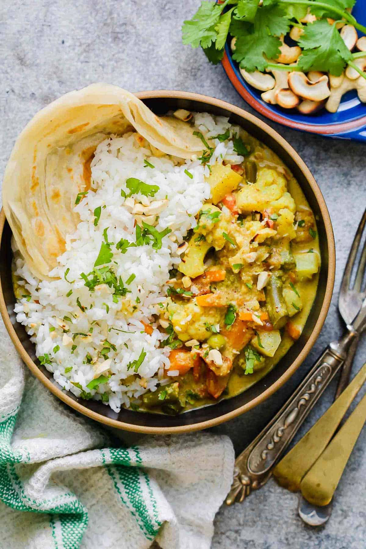 Vegetable Korma Curry served in a bowl with rice, malabar paratha and topped with crunchy cashews