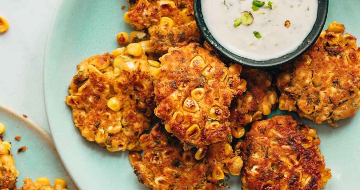 Mexican corn fritters served on a blue plate with a creamy dip on the side