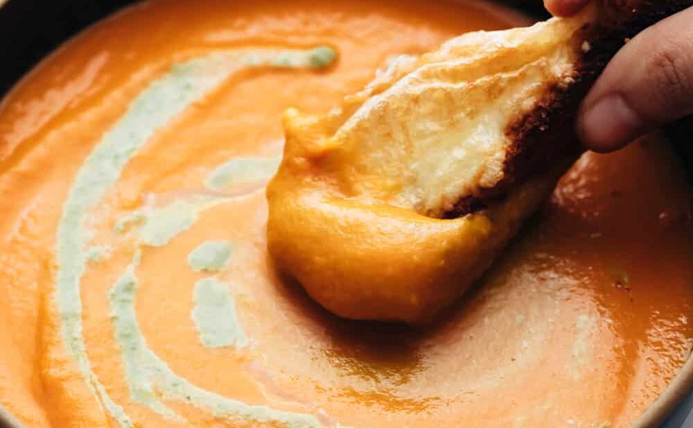 Roasted Tomato Pesto Soup served in a bowl with cheesy bread being dunked into soup