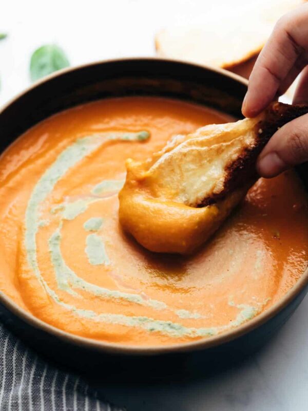 Roasted Tomato Pesto Soup served in a bowl with cheesy bread being dunked into soup