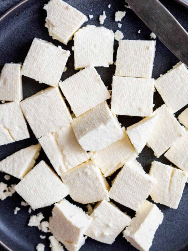 Cubes of paneer served on a grey plate with a knife