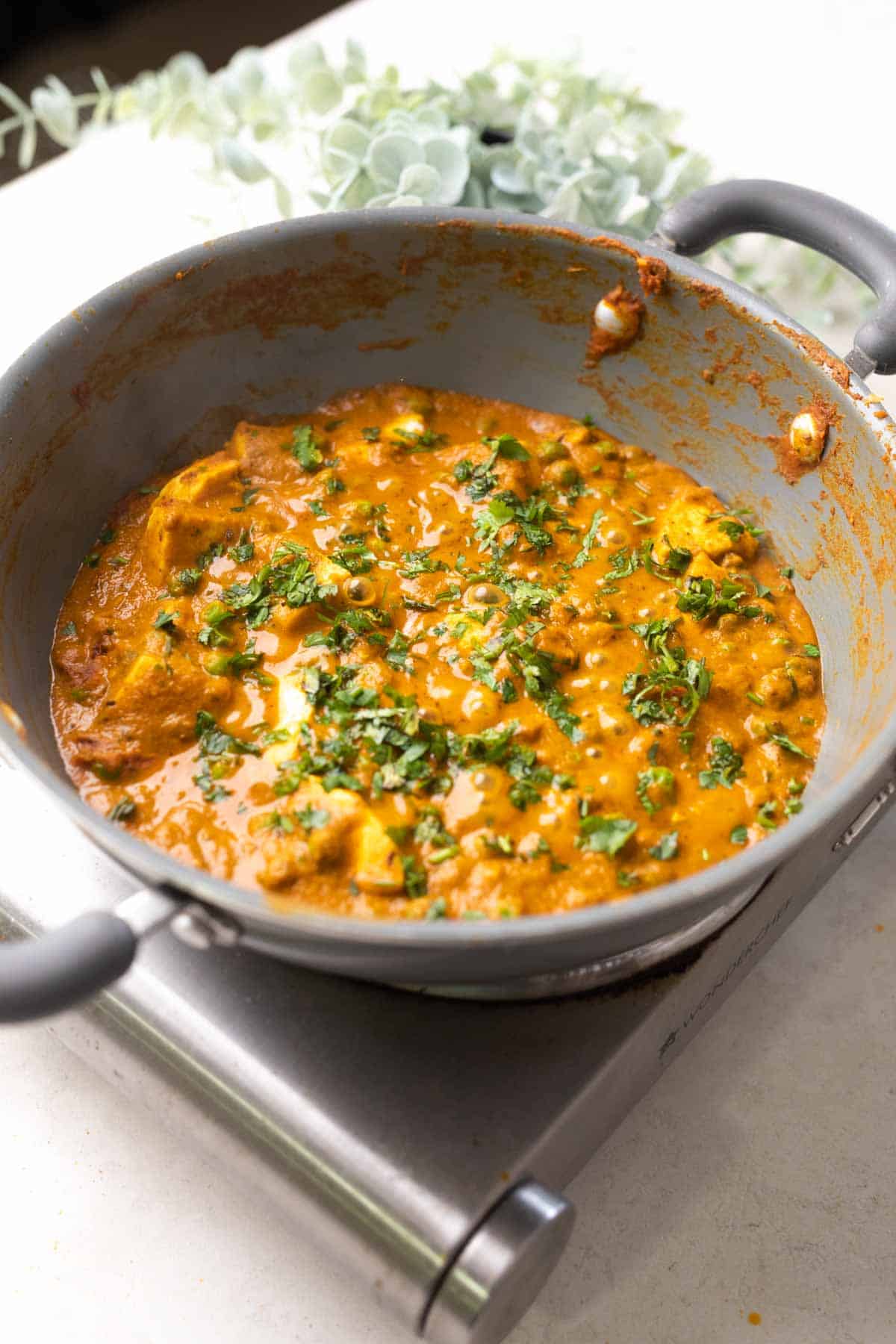 shot of matar paneer gravy in a grey pan with coriander sprinkled on top