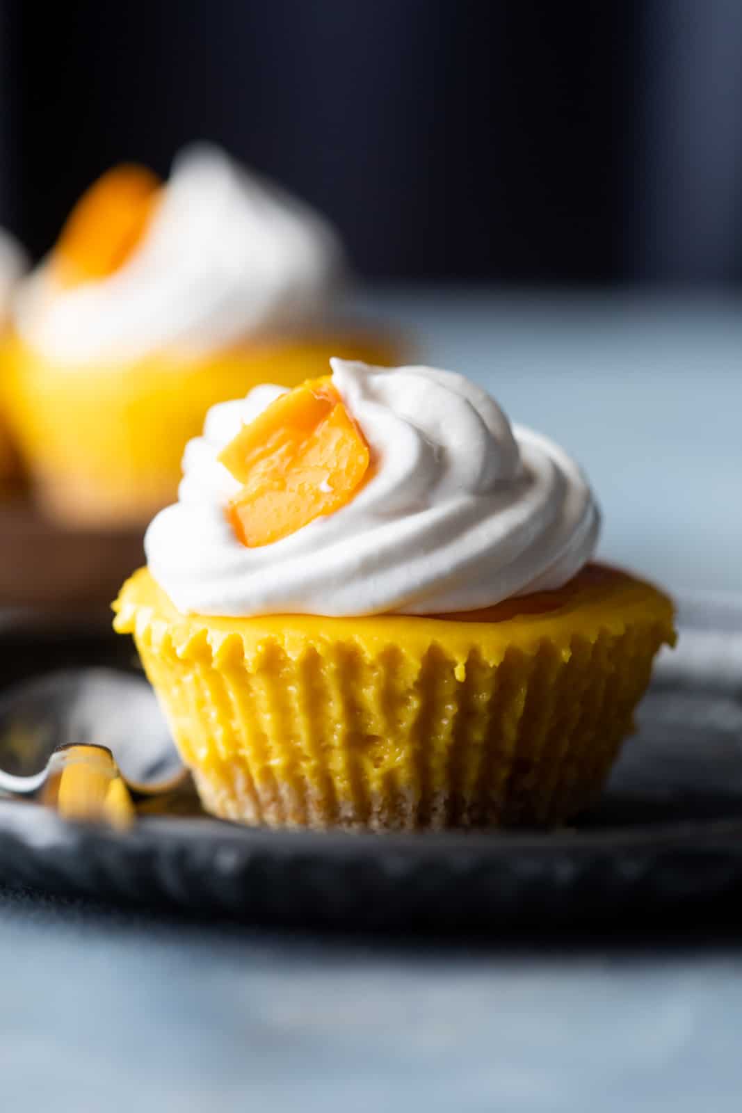 Mini mango cheesecakes served on a plate topped with whipped cream and fresh mangoes