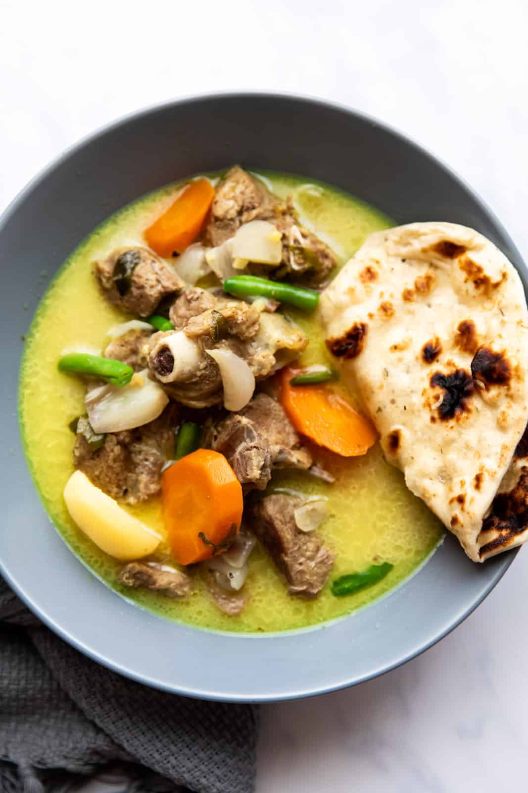 Mutton stew with coconut served in a bowl with naan bread