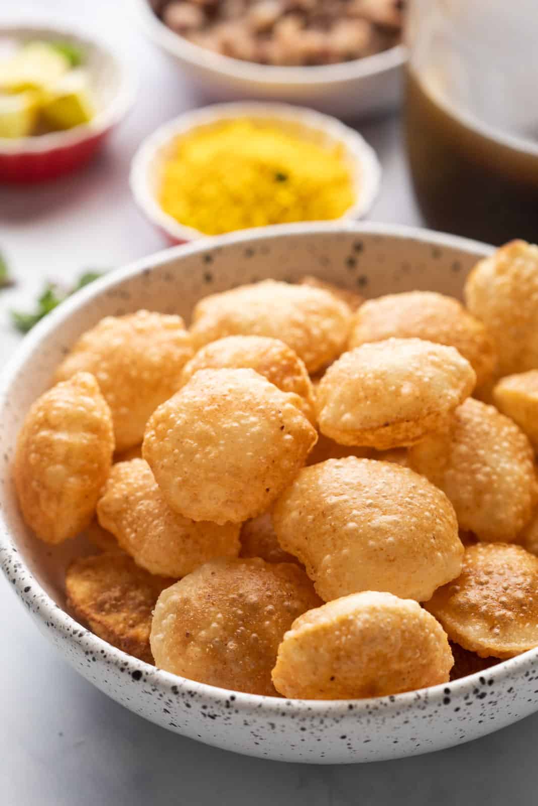 Puris served in a bowl with the pani and filling in the background