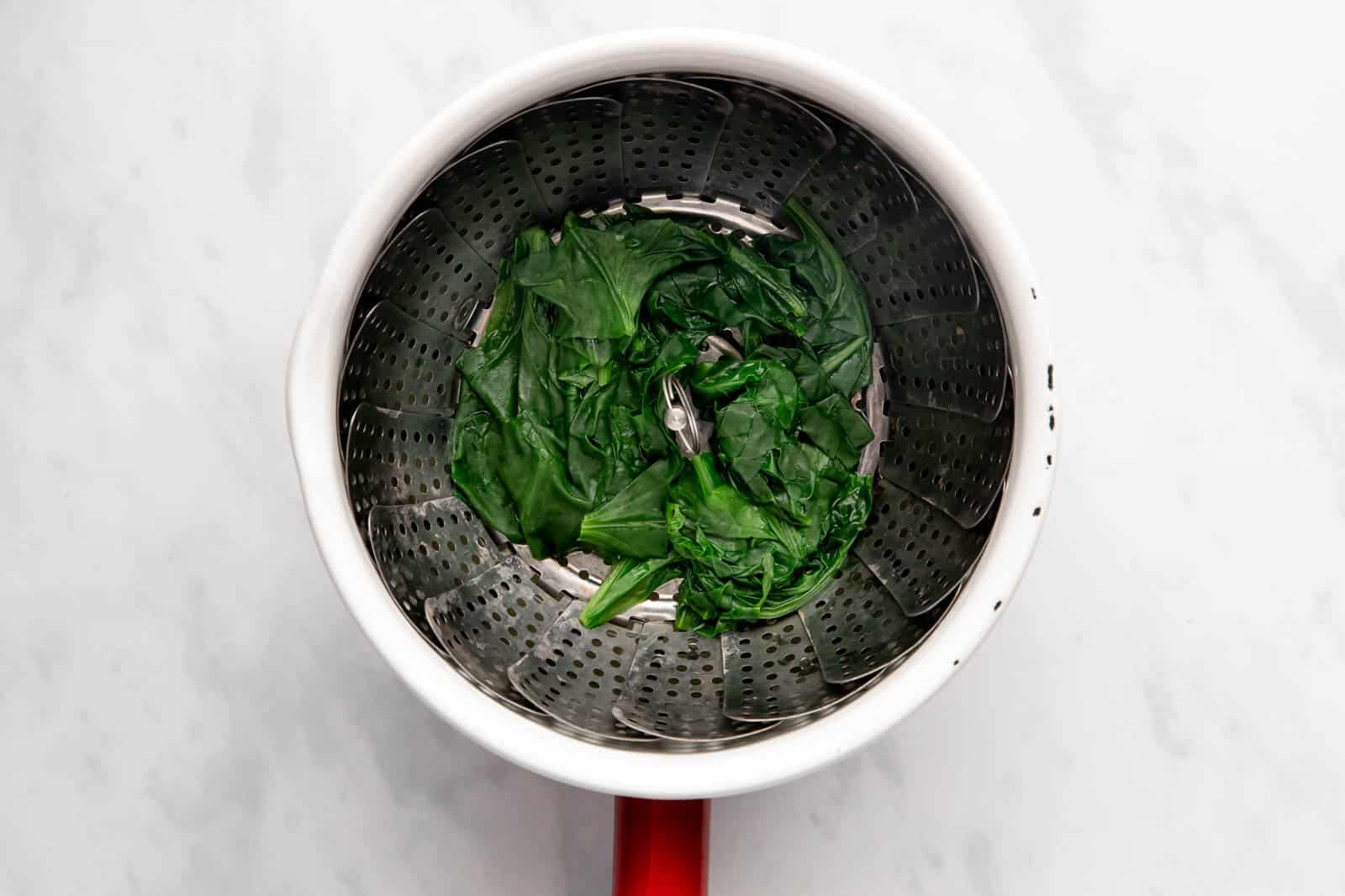 Steaming spinach in a steamer basket till it wilts