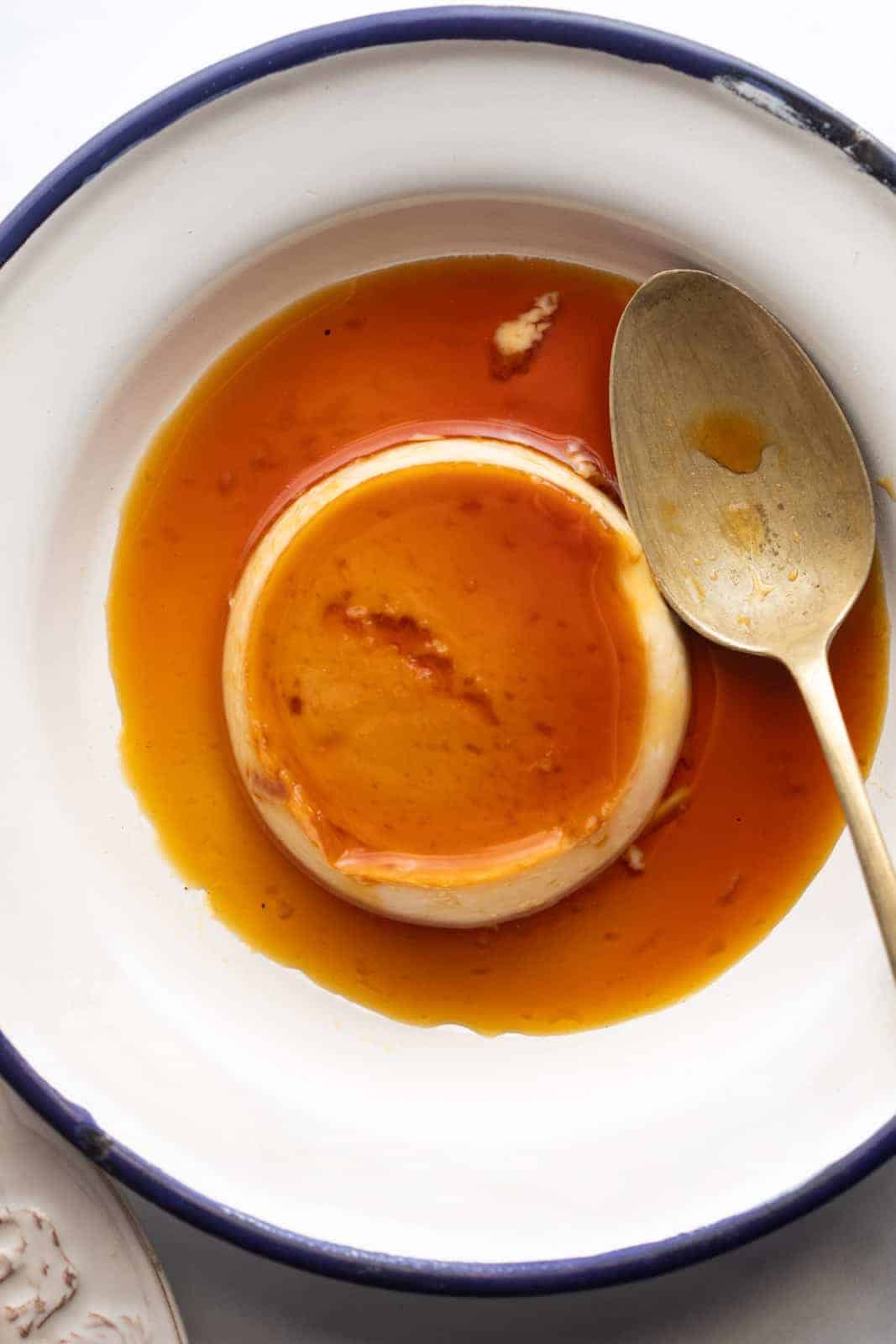 Closeup of coconut caramel custard served on a white plate with a blue edging and a spoon