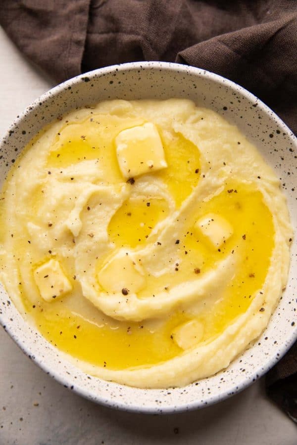 Mashed potatoes served in a white bowl with pools of butter on top