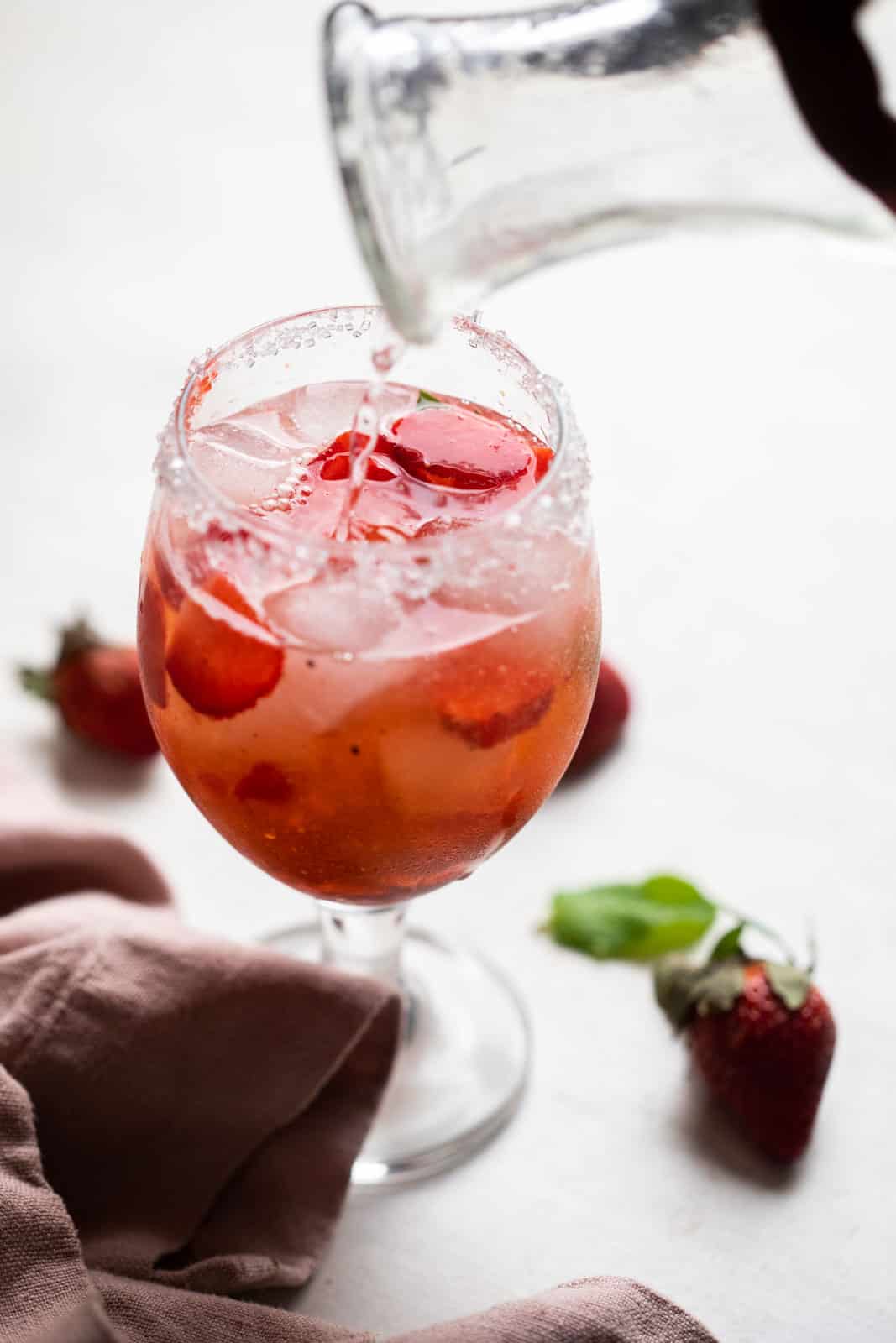 Pouring tonic water into a steam glass with gin, strawberries and ice