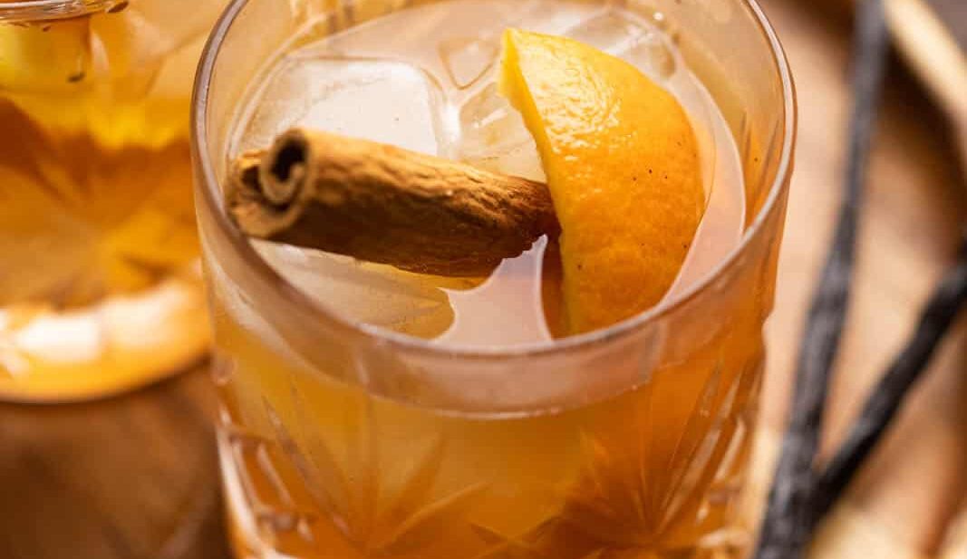 A glass of vanilla cinnamon old fashioned on a tray with vanilla beans on the side