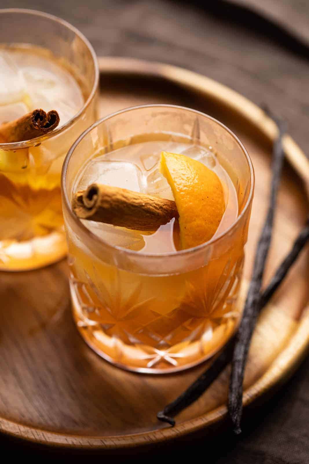 A glass of vanilla cinnamon old fashioned on a tray with vanilla beans on the side