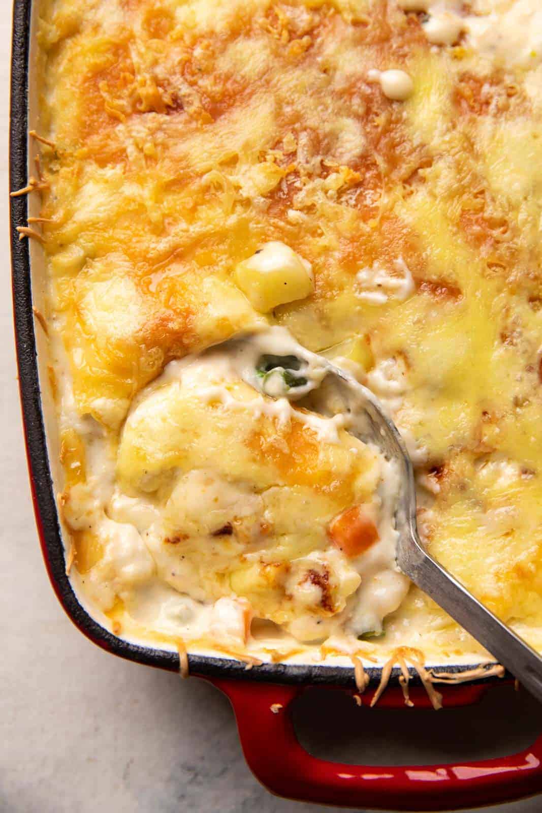 Closeup of a picture showing a spoon serving veg au gratin out of the casserole dish