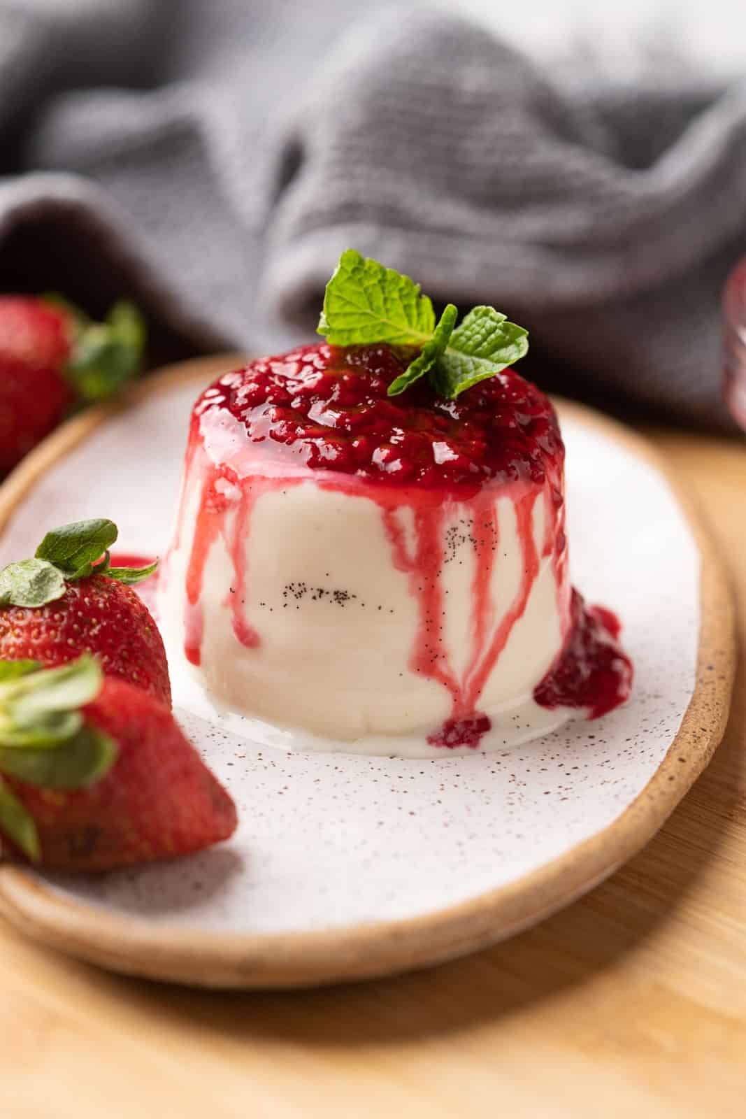 Classic panna cotta with specks of vanilla topped with raspberry coulis served on a white plate
