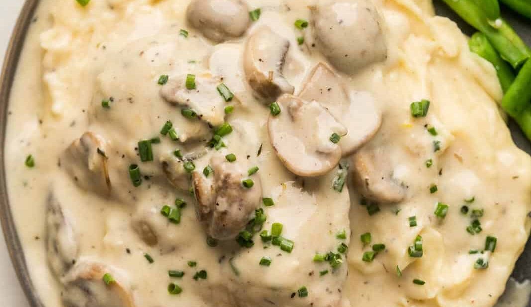 Instant Pot Chicken in mushroom sauce served over a bed of mashed potatoes on a grey plate with steamed green beans