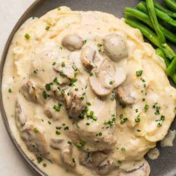 Instant Pot Chicken in mushroom sauce served over a bed of mashed potatoes on a grey plate with steamed green beans