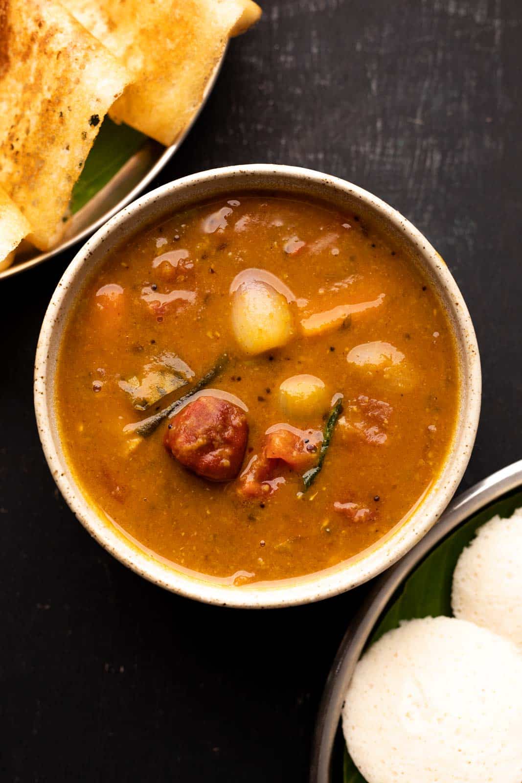 Vegetable sambar served in a brown bowl with a stack of idlis and dosas on the side