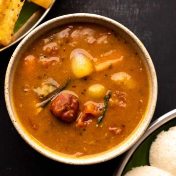 Vegetable sambar served in a brown bowl with a stack of idlis and dosas on the side