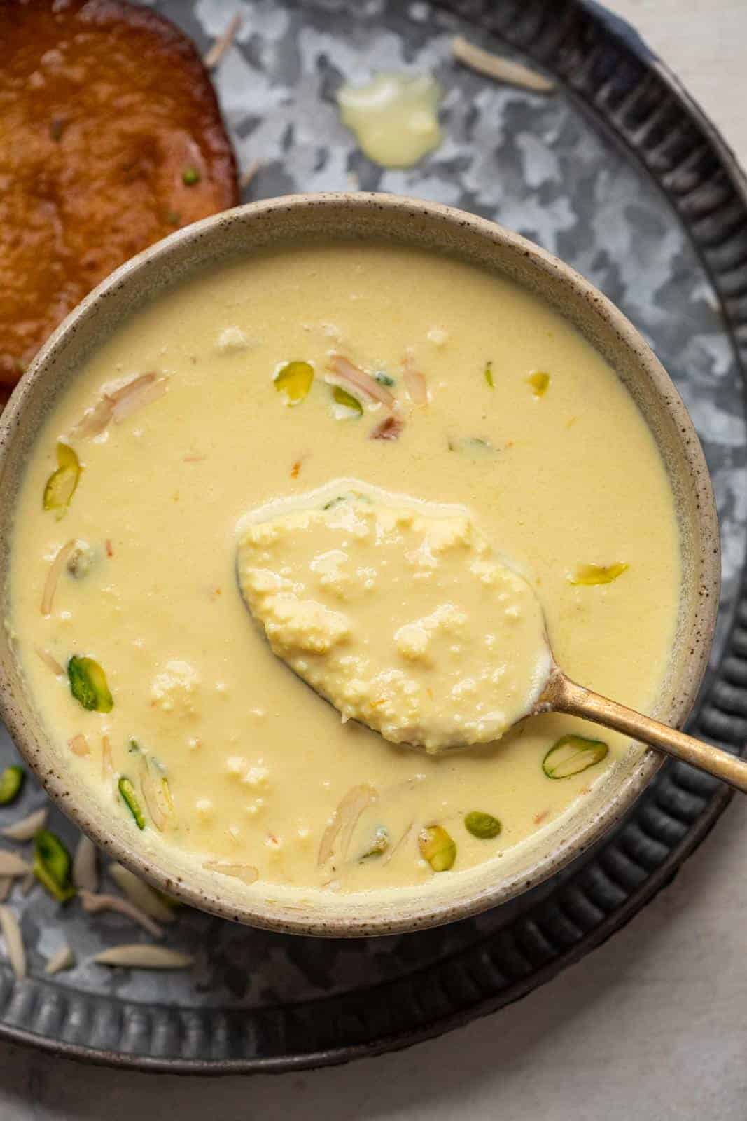 Close up of a spoon of instant rabdi in a brown bowl to show the creamy layers in the rabdi