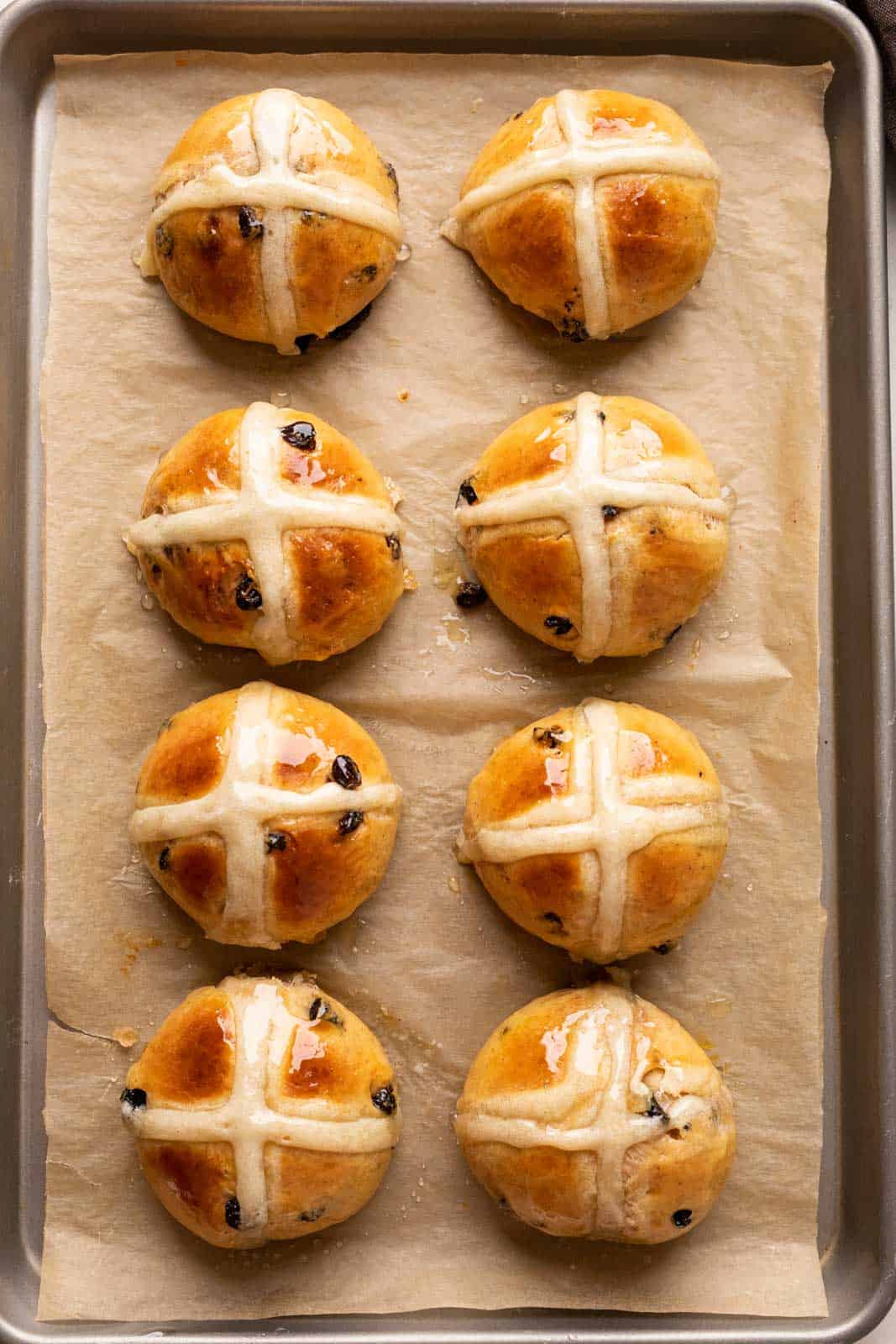 8 Hot Cross Buns on parchment paper on a baking sheet straight from the oven