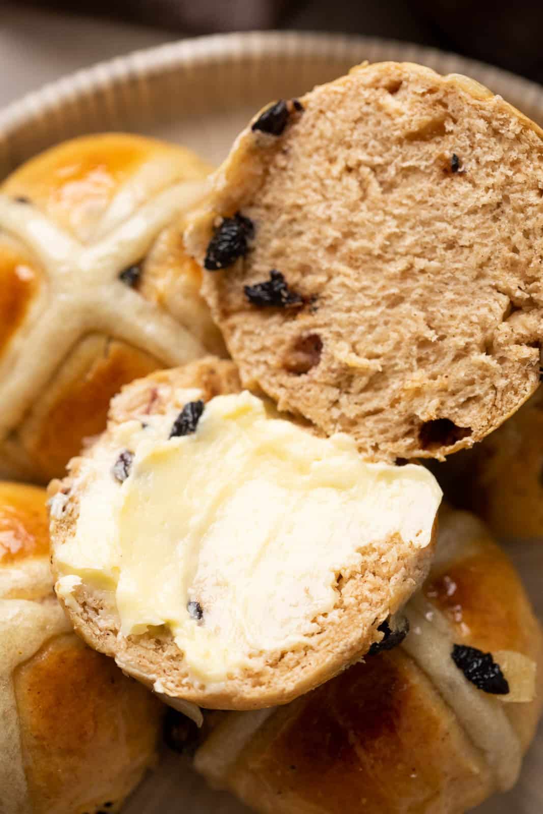 A hot cross bun that has been sliced oven with soft butter slathered on it