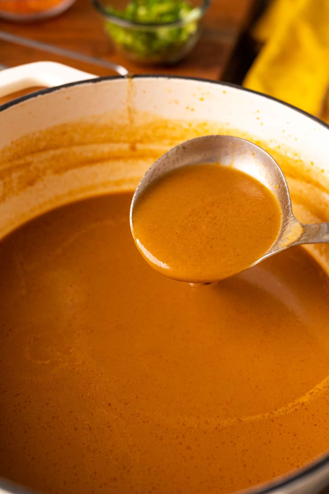 Picture of a ladle pouring the broth to show the creamy, smooth texture of the orange coloured broth