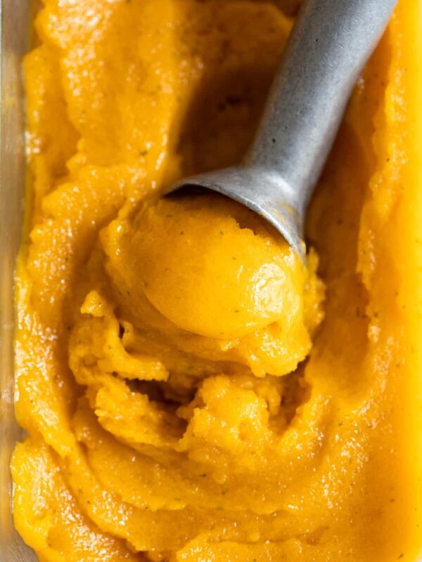 Mango sorbet being scooped out with an ice cream scooper from the container