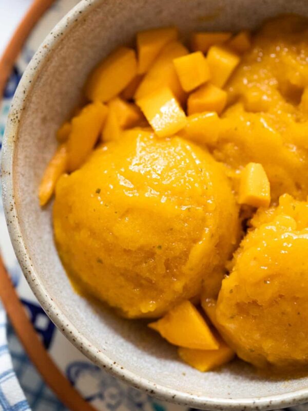 Mango sorbet scoops served in a brown ceramic bowl with diced mangoes
