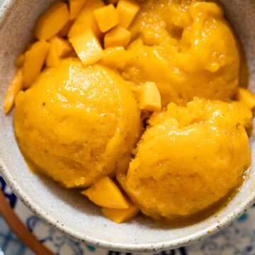 Mango sorbet scoops served in a brown ceramic bowl with diced mangoes
