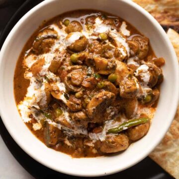 Mushroom masala served in a white bowl with a drizzle of cream on top with paratha on the side