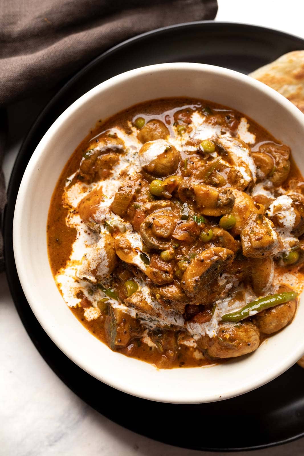 Mushroom masala served in a white bowl with a drizzle of cream on top with paratha on the side