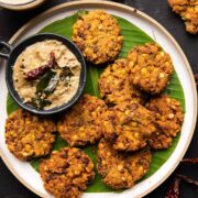 Crispy masala vadas served on a banana leaf lined white plate with coconut chutney on the side