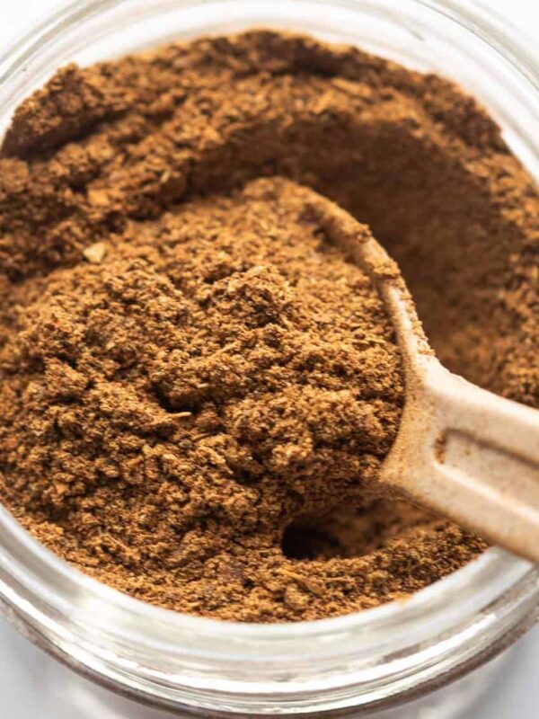 Garam Masala pictured in a glass jar used for storage with a spoon in it
