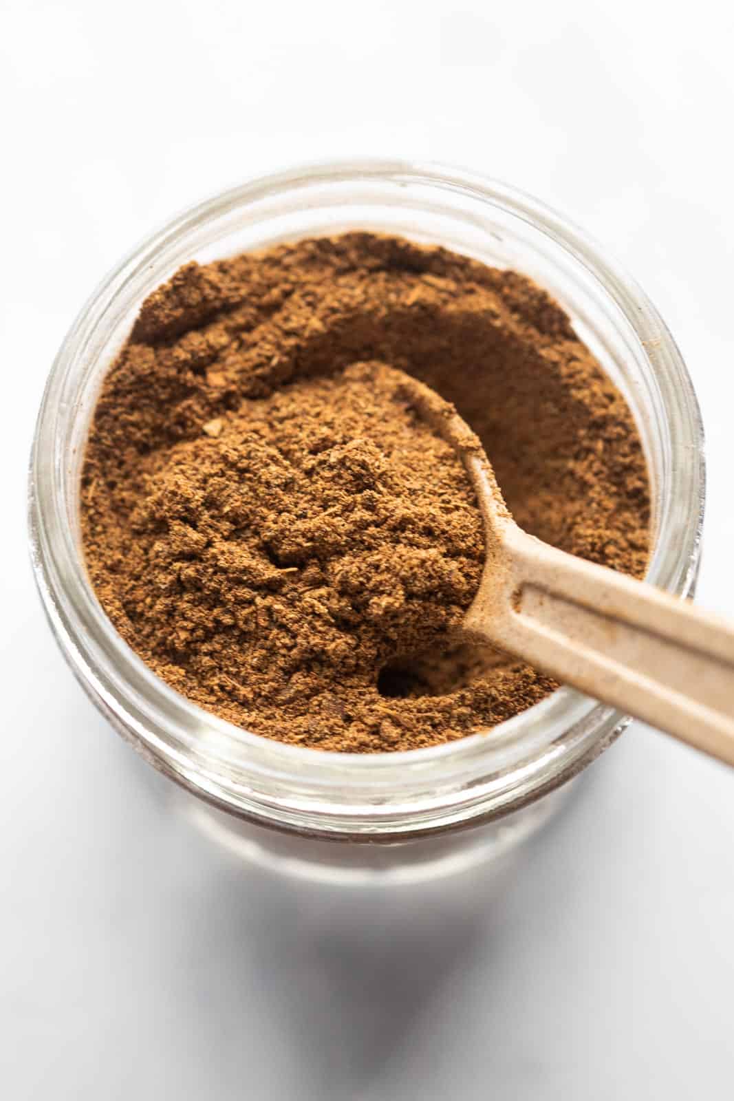Garam Masala pictured in a glass jar used for storage with a spoon in it