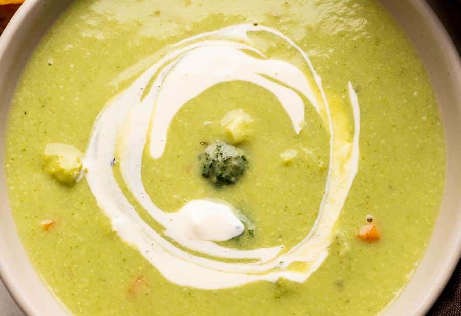 Healthy broccoli soup served in a white bowl with garlic bread on the side