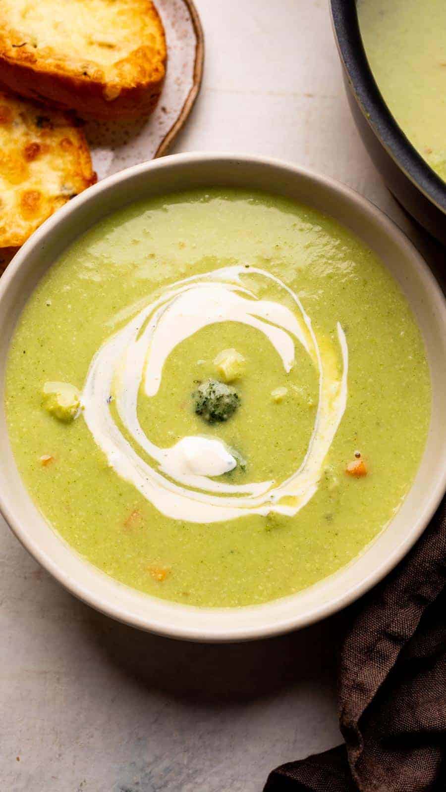 Healthy broccoli soup served in a white bowl with garlic bread on the side