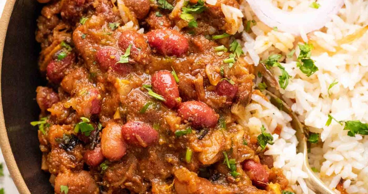 Rajma Masala served in a bowl on top of rice with sliced onions on the side