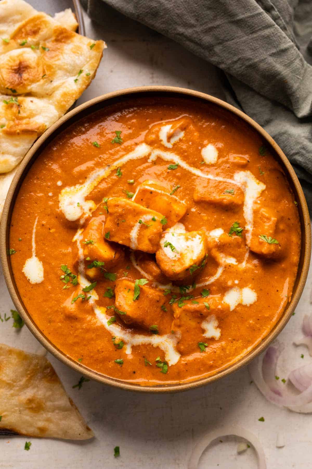 Paneer Butter Masala served in a black bowl with naan and sliced onions on the side