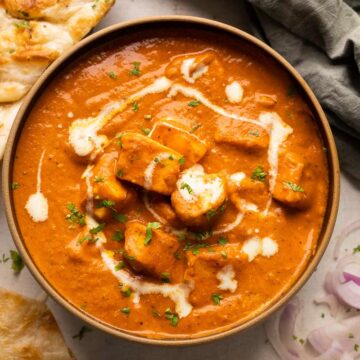Paneer Butter Masala served in a black bowl with naan and sliced onions on the side