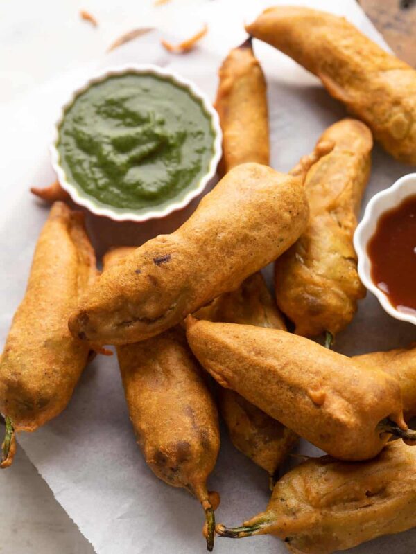 Mirchi bajjis served on parchment paper with green chutney and ketchup