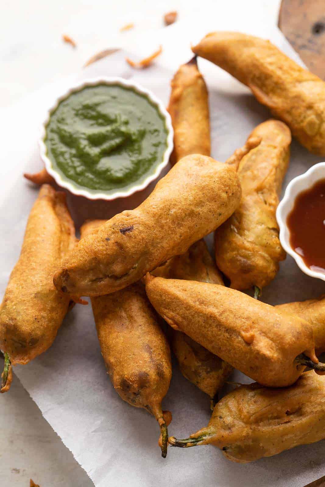 Mirchi bajjis served on parchment paper with green chutney and ketchup