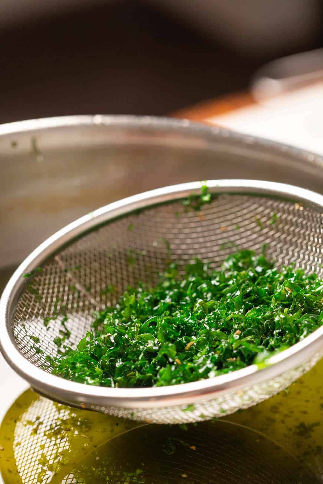 Crispy fried spinach being taken out of hot oil in a strainer