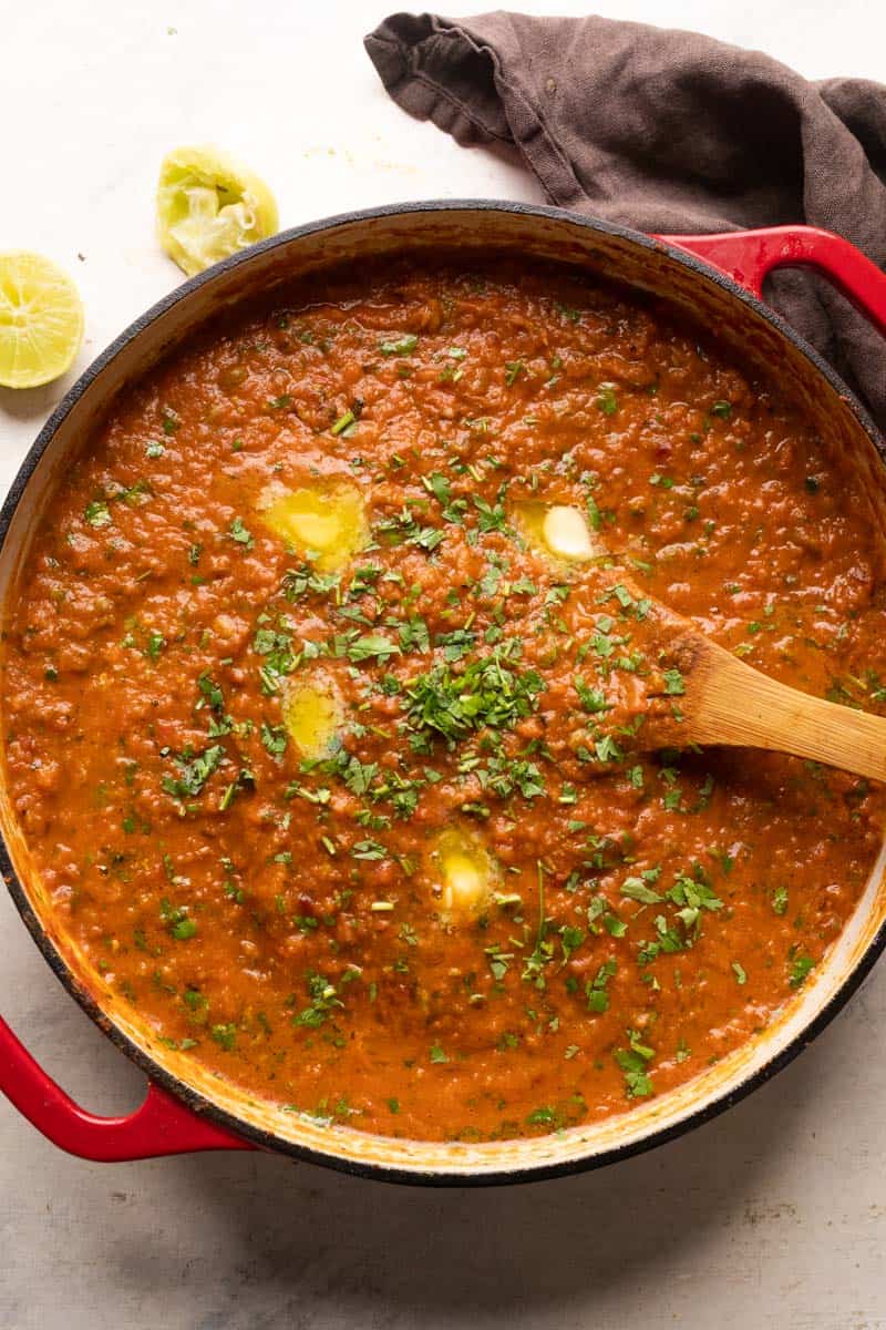 Pav Bhaji served in a large red shallow pan in which it was cooked with a wooden ladle