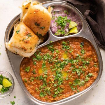 Pav Bhaji served in a steel plate with ladi pav, onions and coriander on the side