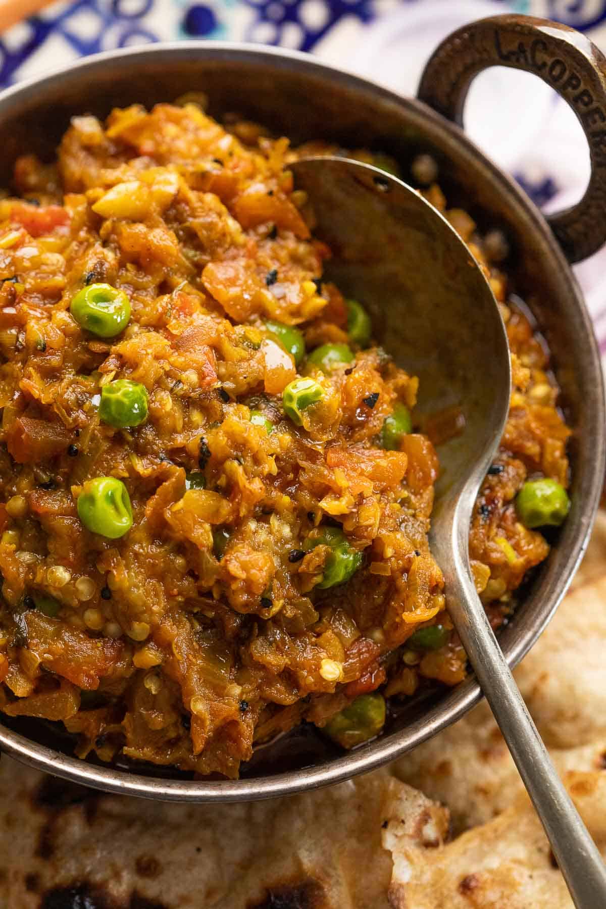 Baingan Bharta served in a copped kadhai with tandoori roti and sliced onions on the side