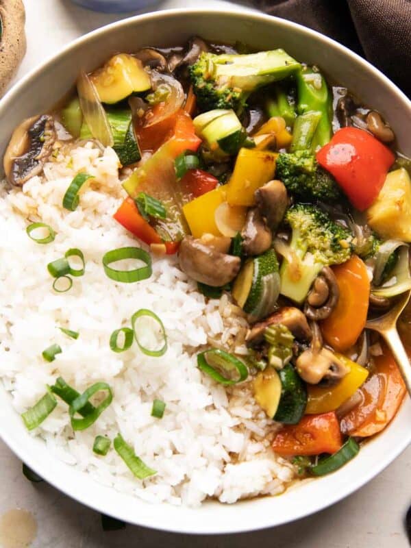 Chinese veg stir fry served in a white bowl with rice on the side sprinkled with spring onions