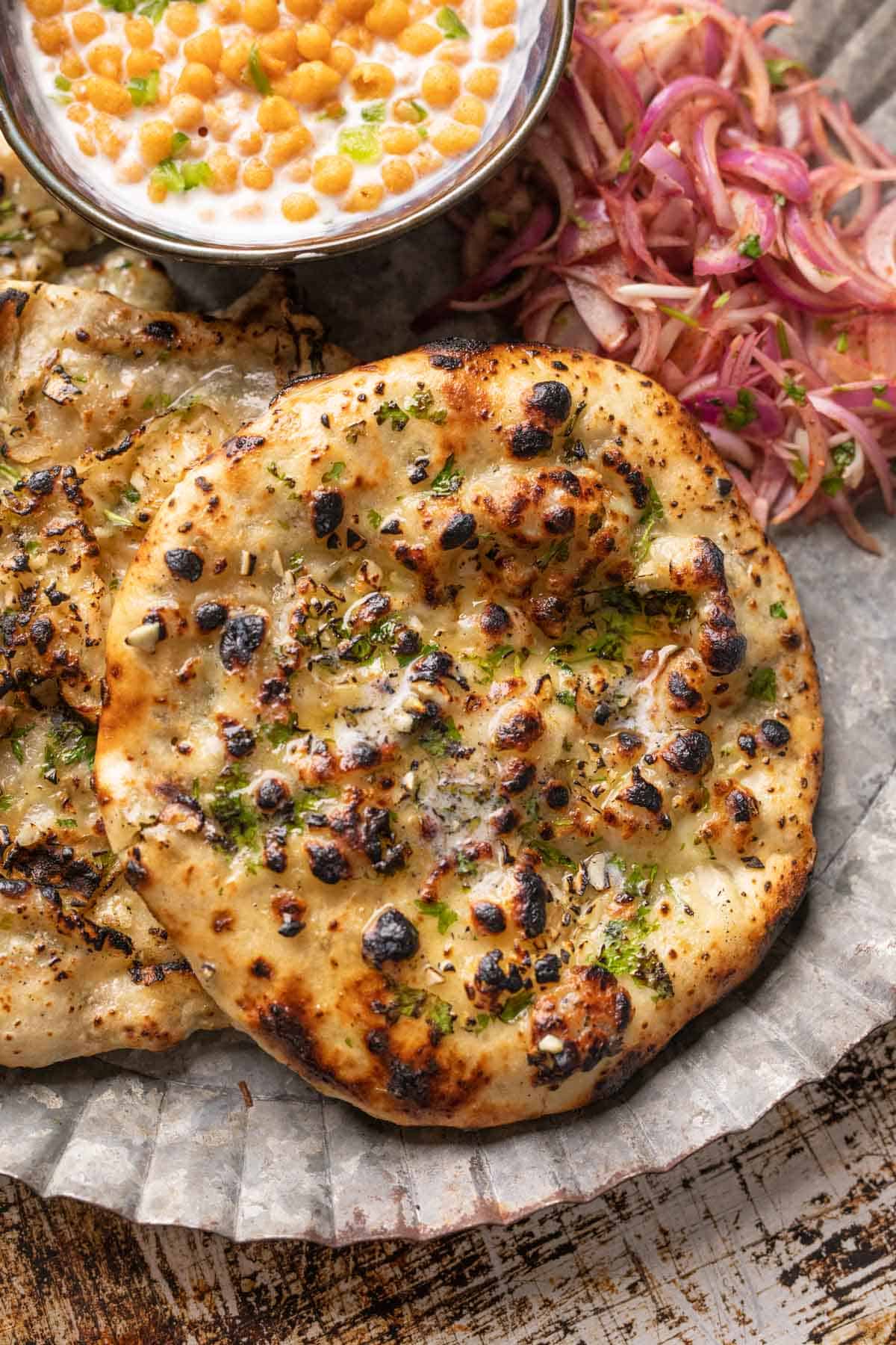 Garlic cheese kulcha served on a plate with pickled onions and boondi raita on the side