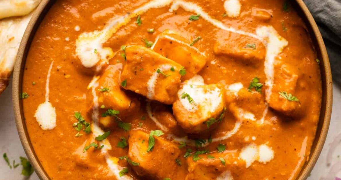 Paneer Butter Masala served in a brown bowl with naan and onions on the side