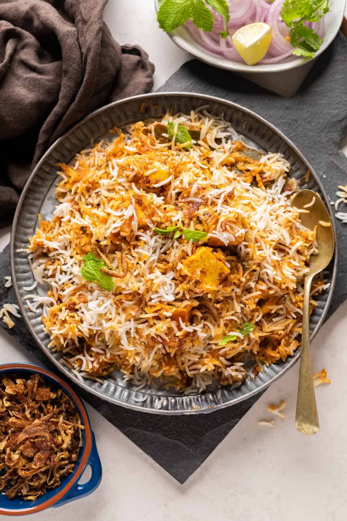 Paneer Biryani served on a grey plate with fried onions on the side