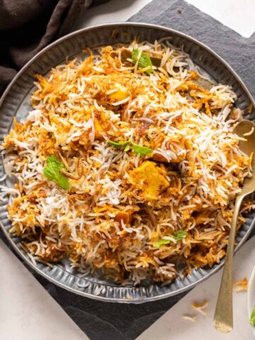 Paneer Biryani served on a grey plate with fried onions on the side