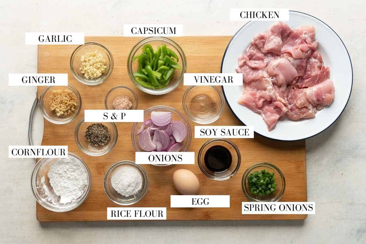 All the ingredients for salt and pepper chicken laid out a wooden board with text to identify them